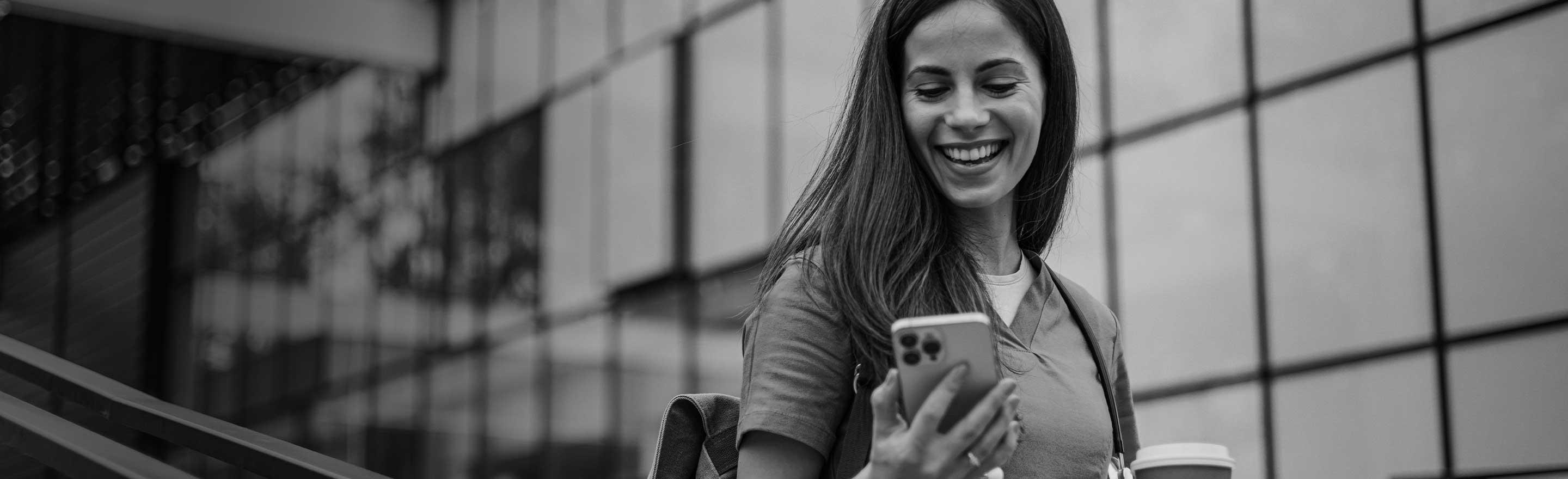 Woman in scrubs, smiling while looking down at her mobile phone